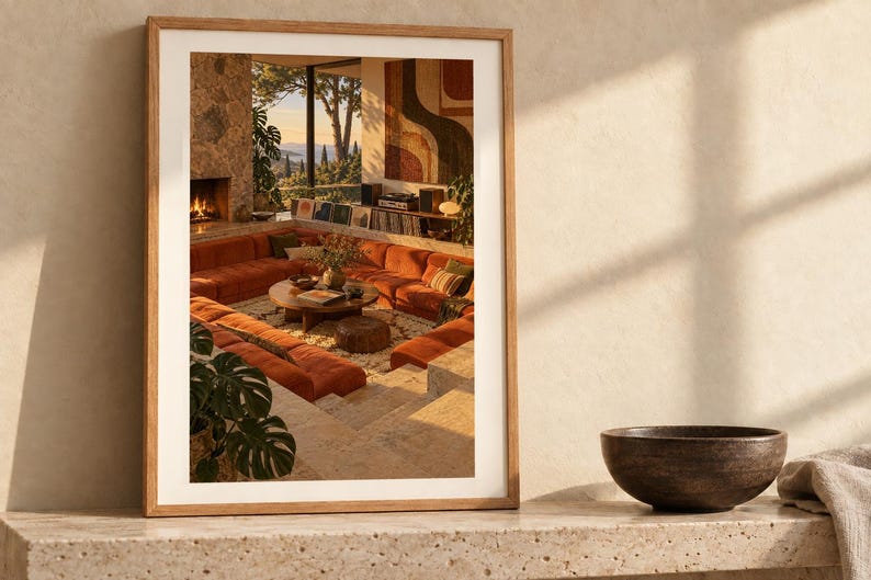 May include: A framed wall art print featuring a sunken living room with a large orange sectional sofa, a round wooden coffee table, a stone fireplace, and floor-to-ceiling windows overlooking a landscape, all set within a light-toned wooden frame.