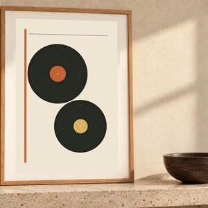 May include: A framed wall art print featuring two black vinyl records on a cream background. The top record has an orange center label, and the bottom record has a yellow center label. A vertical orange line runs along the left side.