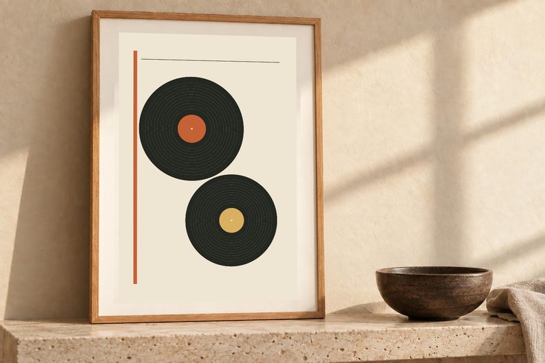May include: A framed wall art print featuring two black vinyl records on a cream background. The top record has an orange center label, and the bottom record has a yellow center label. A vertical orange line runs along the left side.