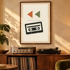 May include: A framed wall art print featuring a black cassette tape graphic centered below a small orange triangle and a green triangle on a cream background. The print is displayed in a dark brown frame hanging on a textured wall.