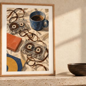 May include: A framed wall art print featuring two clear plastic cassette tapes with unspooled brown magnetic tape, a blue ceramic mug filled with dark coffee, a solid orange rectangular box, and a blue and yellow square object on a white fabric.