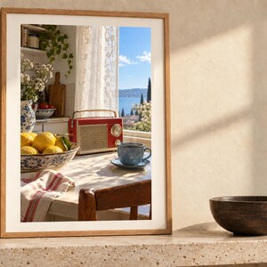 May include: A framed wall art print featuring a kitchen scene with a red radio, a bowl of yellow lemons, and a blue teacup on a table. The view through the window shows a blue sea and cypress trees. The frame is light wood with a white mat border.