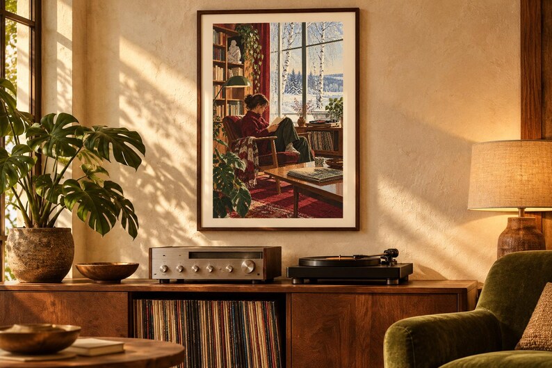 Puede incluir: Una l&aacute;mina de arte enmarcada que representa a una persona leyendo en un sill&oacute;n rojo dentro de una habitaci&oacute;n con estanter&iacute;as, una l&aacute;mpara verde y vistas a un paisaje nevado a trav&eacute;s de un gran ventanal, sobre un mueble de madera.