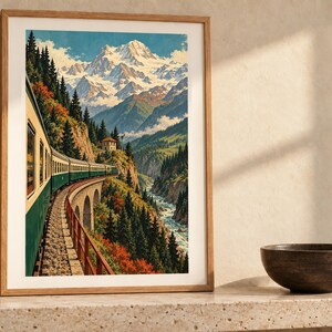 May include: A framed vertical wall art print depicting a green and cream train traveling along a stone viaduct through a mountain valley. The scene features snow-capped peaks, dense evergreen forests, and a river flowing below the tracks.