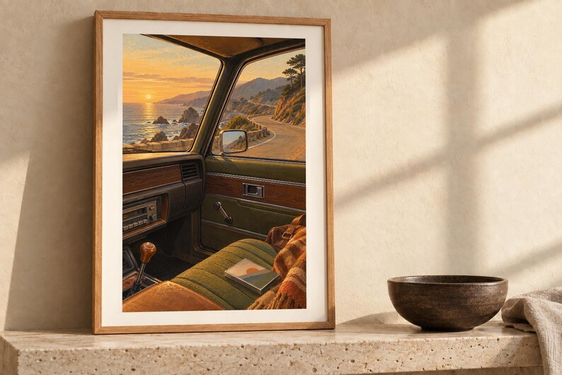 Puede incluir: Una l&aacute;mina de arte enmarcada que representa el interior de un coche antiguo con vistas a una carretera costera al atardecer. La escena muestra un asiento tapizado en verde, una palanca de cambios de madera y el mar y acantilados.