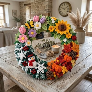 May include: A seasonal crochet wreath featuring a transition from spring and summer flowers like sunflowers and tulips to autumn pumpkins and leaves, ending with winter elements including a snowman, snowflakes, and red berries.