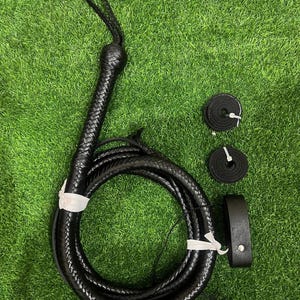 Può includere: Una frusta in pelle intrecciata nera con un laccio da polso sull'impugnatura, avvolta in forma circolare e fissata con lacci bianchi. Sono inclusi due piccoli rotoli circolari di pelle e una cinghia in pelle nera con un rivetto in metallo.