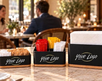 Puede incluir: Un juego de cuatro organizadores de mesa en negro mate con bases de madera clara, cada uno con el texto Your Logo. El juego incluye un soporte para sobres de azúcar, un organizador de condimentos, un servilletero y un soporte con dos botellas.