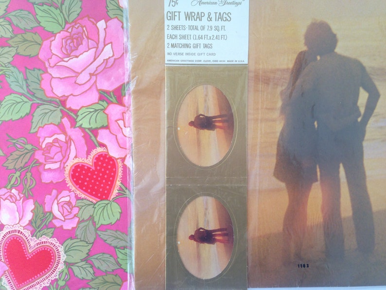 May include: Gift wrap and tags set. The gift wrap features a pink rose and heart design. The tags have an oval image of a couple on a beach. The packaging includes the text "Gift Wrap & Tags" and "American Greetings".