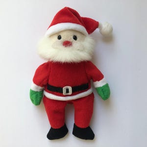 May include: A plush Santa Claus doll, with a red suit, hat, and boots. The doll has a white beard, a black belt with a silver buckle, and green gloves. The hat has a white trim and a white pom-pom.