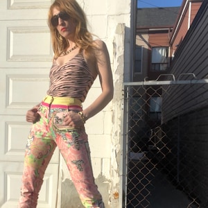 Pode incluir: Uma mulher vestindo um top halter de estampa de zebra com um cinto amarelo, cal&ccedil;as estampadas em rosa e verde e sand&aacute;lias de salto alto douradas.