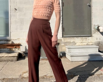 Calças vintage de Katharine Hepburn, anos 1940, em gabardine de lã marrom, pernas largas, cintura alta marcada e fechamento lateral com botões.