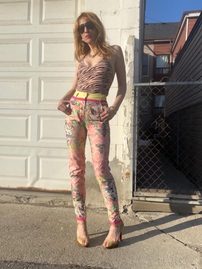 Pode incluir: Uma mulher vestindo uma cal&ccedil;a de estampa floral rosa e branca com um cinto amarelo e um top de estampa de zebra marrom. Ela est&aacute; usando &oacute;culos de sol e saltos dourados.