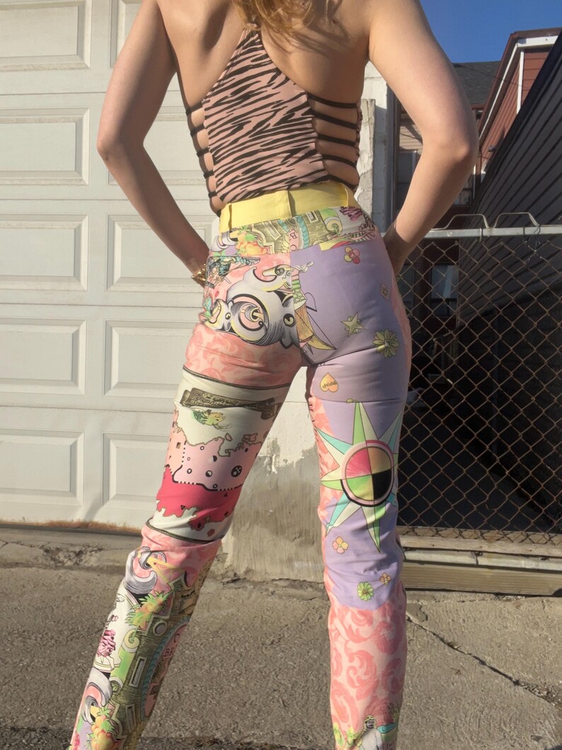 Pode incluir: Uma cal&ccedil;a de cintura alta com um design de patchwork colorido. A cal&ccedil;a &eacute; feita de um tecido leve e tem um caimento solto. O design apresenta uma variedade de padr&otilde;es, incluindo flores, estrelas e formas geom&eacute;tricas. A cal&ccedil;a &eacute; uma mistura vibrante de rosa, roxo, amarelo e verde.