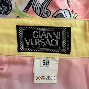Pode incluir: Uma saia amarela e rosa com uma cintura estampada em preto e branco. A saia tem uma etiqueta que diz "Gianni Versace Couture Made in Italy". A etiqueta de tamanho diz "38".