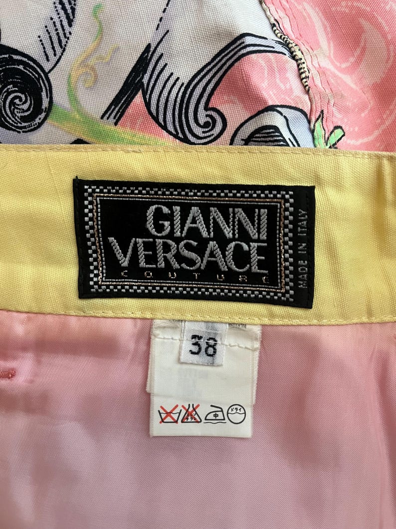 Pode incluir: Uma saia amarela e rosa com uma cintura estampada em preto e branco. A saia tem uma etiqueta que diz "Gianni Versace Couture Made in Italy". A etiqueta de tamanho diz "38".