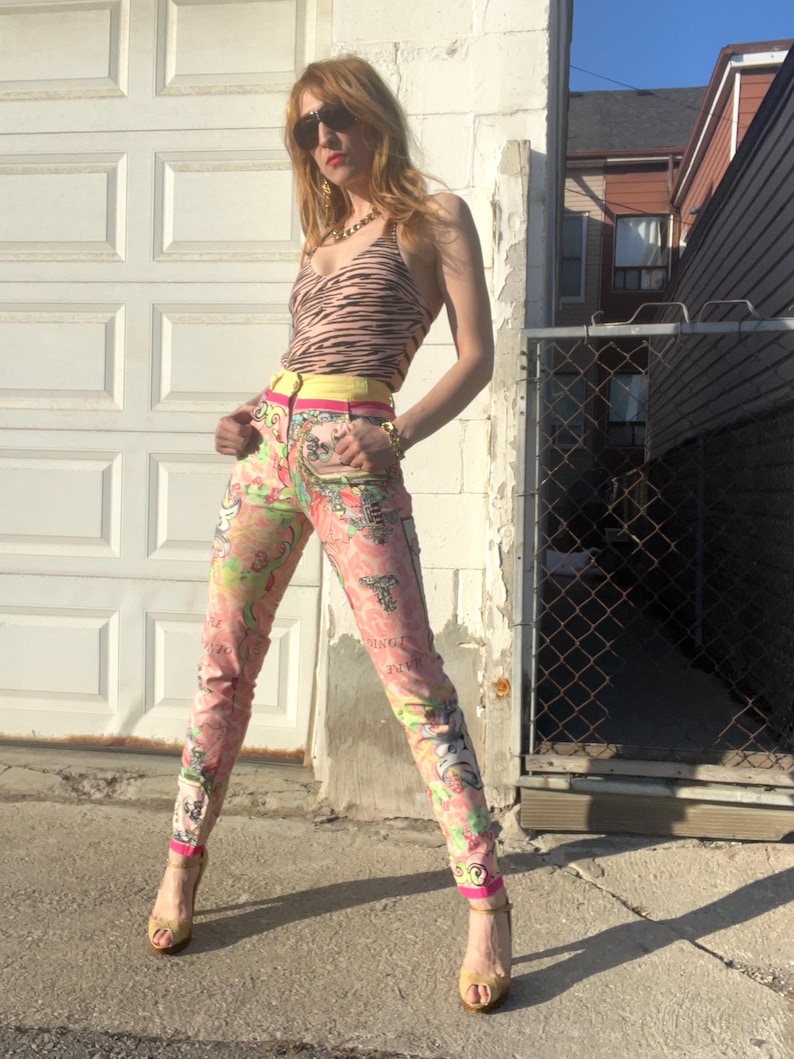 Pode incluir: Uma mulher vestindo um top halter de estampa de zebra com um cinto amarelo, cal&ccedil;as estampadas em rosa e verde e sand&aacute;lias de salto alto douradas.