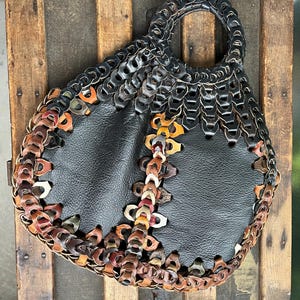 May include: A black leather handbag with a unique design. The bag is made of leather strips that are woven together to create a pattern. The bag has a single handle and a flap closure.