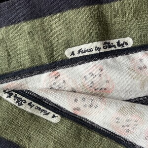 May include: Close-up of a green and black striped fabric with two labels. The top label reads "A Fabro by Shin-Eyo". The bottom label reads "x ongos by Shin-Eyo".