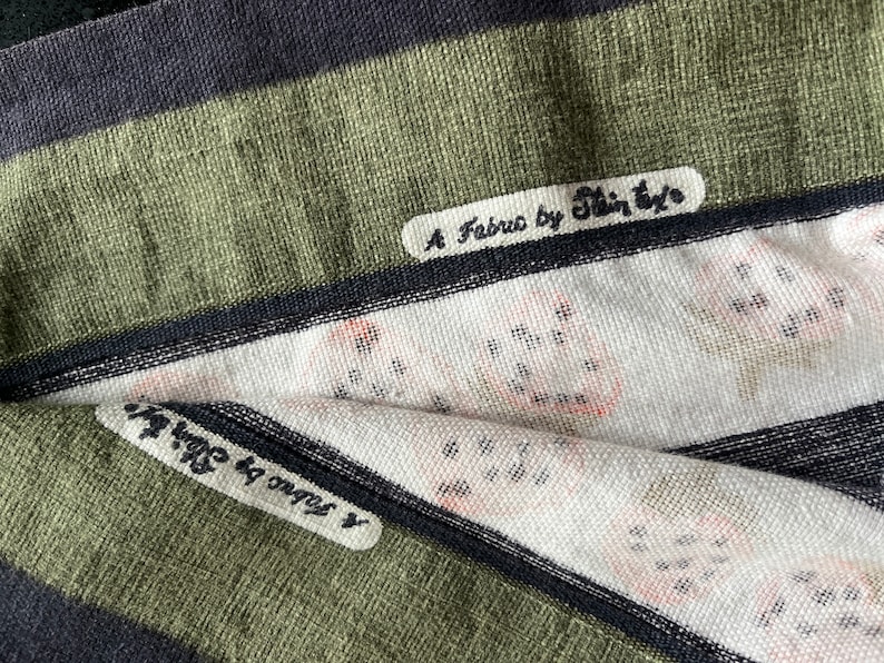 May include: Close-up of a green and black striped fabric with two labels. The top label reads "A Fabro by Shin-Eyo". The bottom label reads "x ongos by Shin-Eyo".