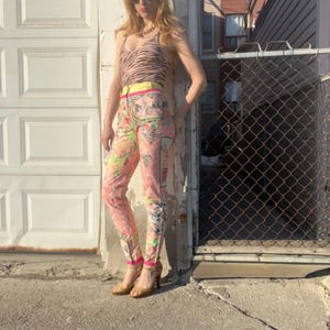 Pode incluir: Uma mulher vestindo um top de tanque de estampa de zebra, cal&ccedil;as de cintura alta com estampa floral colorida e sand&aacute;lias de salto alto douradas. As cal&ccedil;as t&ecirc;m uma cintura amarela e uma estampa floral rosa e verde.