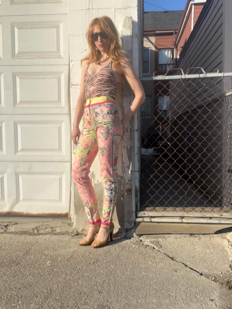 Pode incluir: Uma mulher vestindo um top de tanque de estampa de zebra, cal&ccedil;as de cintura alta com estampa floral colorida e sand&aacute;lias de salto alto douradas. As cal&ccedil;as t&ecirc;m uma cintura amarela e uma estampa floral rosa e verde.
