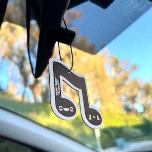 May include: A black and white car air freshener shaped like a musical note with the text "Band Camp Buddies." The note has a smiling face with pink cheeks.
