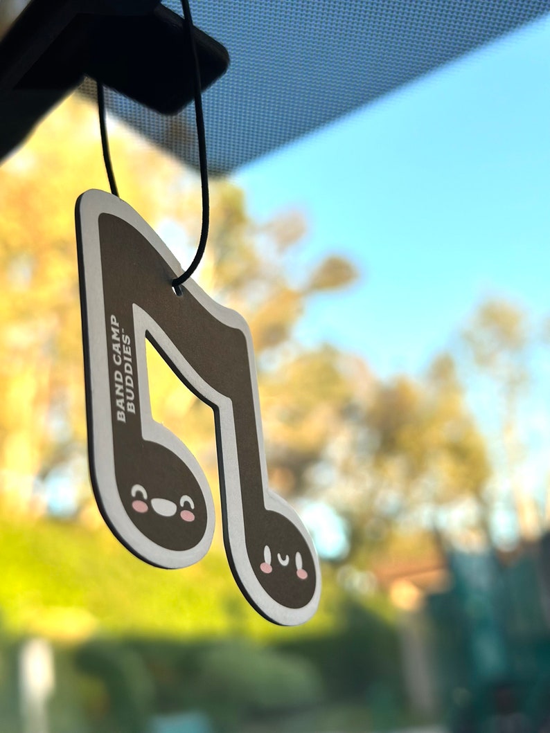 May include: A brown musical note car air freshener with a cute cartoon face. The air freshener says "Band Camp! Buddies!" on the back.