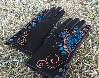 Op de afbeelding: Een paar zwarte leren handschoenen met een decoratief ontwerp met blauwe en oranje spiralen. De handschoenen hebben drukknopen aan de pols.