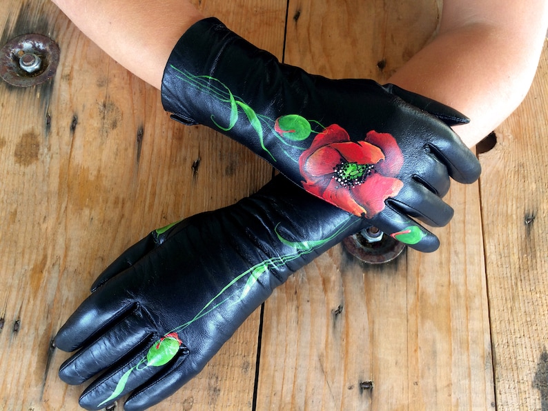 K&ouml;nnte beinhalten: Ein Paar schwarze Lederhandschuhe mit einer roten Mohnblume, die auf die R&uuml;ckseite eines Handschuhs gemalt ist. Die Blume hat gr&uuml;ne Bl&auml;tter und eine schwarze Mitte.