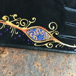 Peut inclure: Gant de cuir noir avec un motif dor&eacute; et violet. Le motif repr&eacute;sente un &oelig;il stylis&eacute; avec des volutes et des points.