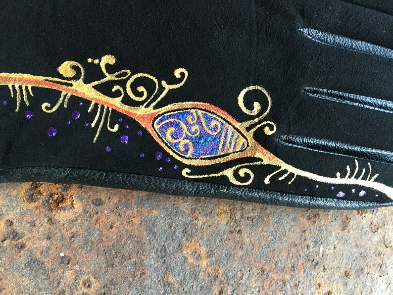 Peut inclure: Gant de cuir noir avec un motif dor&eacute; et violet. Le motif repr&eacute;sente un &oelig;il stylis&eacute; avec des volutes et des points.