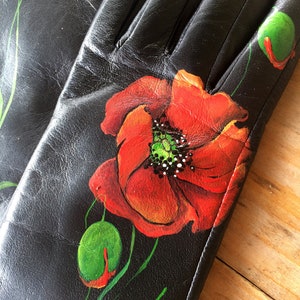K&ouml;nnte beinhalten: Schwarze Lederhandschuhe mit handbemaltem Mohnblumenmuster. Die Blume ist rot mit gr&uuml;nem Zentrum und gr&uuml;nen Bl&auml;ttern.