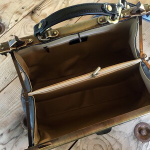May include: Open vintage-style doctor's bag with a black leather handle and brass hardware. The bag has a beige fabric lining and a zippered compartment.