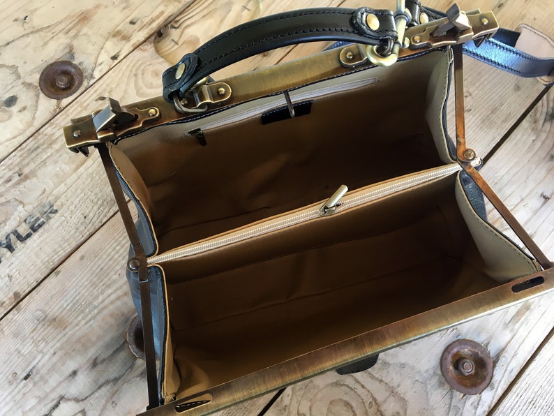 May include: Open vintage-style doctor's bag with a black leather handle and brass hardware. The bag has a beige fabric lining and a zippered compartment.
