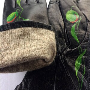 K&ouml;nnte beinhalten: Schwarze Lederhandschuhe mit gr&uuml;nem und rotem Blumendesign. Die Handschuhe haben einen braunen Strickbund.