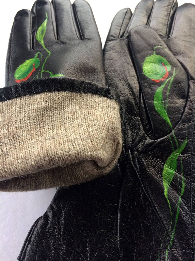 K&ouml;nnte beinhalten: Schwarze Lederhandschuhe mit gr&uuml;nem und rotem Blumendesign. Die Handschuhe haben einen braunen Strickbund.