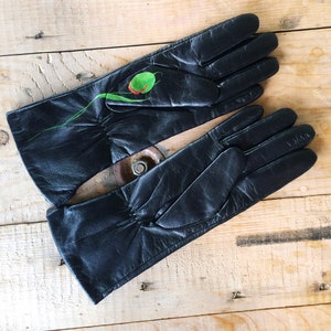 K&ouml;nnte beinhalten: Ein Paar schwarze Lederhandschuhe mit einem gr&uuml;nen und roten Blumendesign auf einem Handschuh.