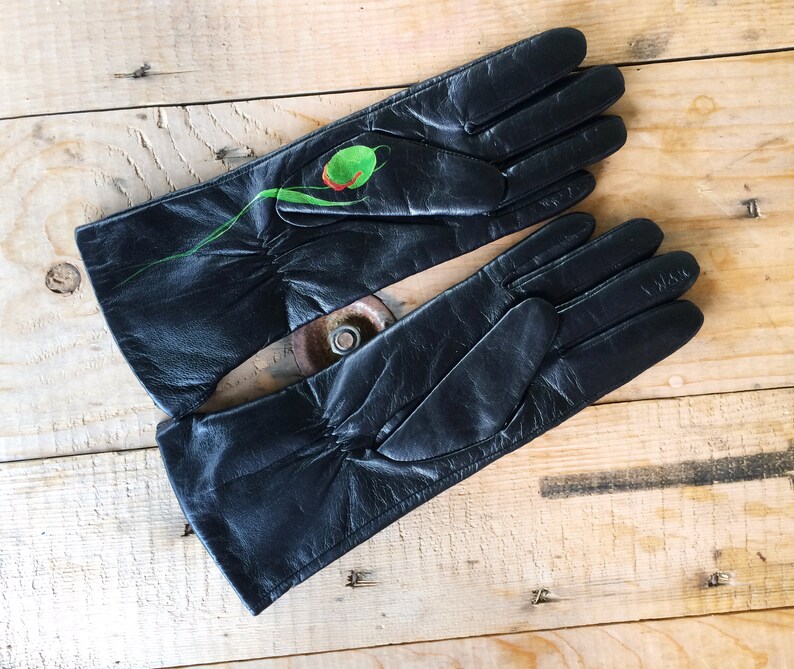 K&ouml;nnte beinhalten: Ein Paar schwarze Lederhandschuhe mit einem gr&uuml;nen und roten Blumendesign auf einem Handschuh.