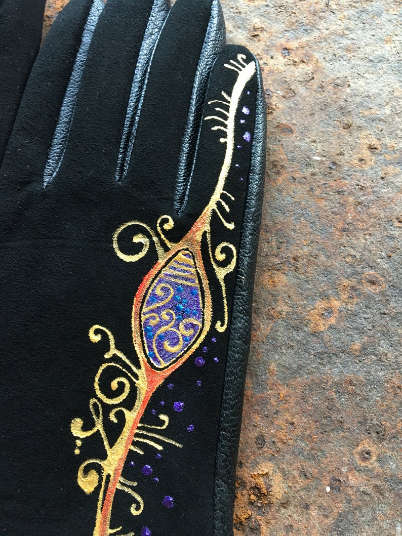 Peut inclure: Gants en cuir noir avec un motif dor&eacute; et violet sur le dos de la main. Le motif repr&eacute;sente une plume stylis&eacute;e avec des volutes et des points.