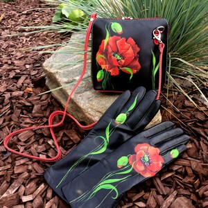 K&ouml;nnte beinhalten: Eine schwarze Lederhandtasche und passende Handschuhe mit einem roten Mohnblumenmuster. Die Handtasche hat einen roten Riemen und einen silbernen Verschluss. Die Handschuhe sind lang und haben auf jedem Handschuh eine rote Mohnblume.