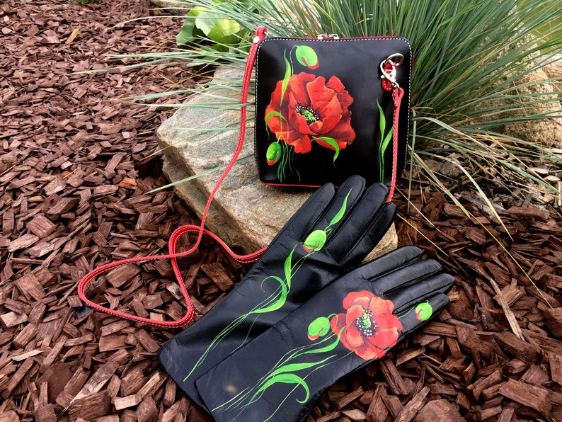 K&ouml;nnte beinhalten: Eine schwarze Lederhandtasche und passende Handschuhe mit einem roten Mohnblumenmuster. Die Handtasche hat einen roten Riemen und einen silbernen Verschluss. Die Handschuhe sind lang und haben auf jedem Handschuh eine rote Mohnblume.