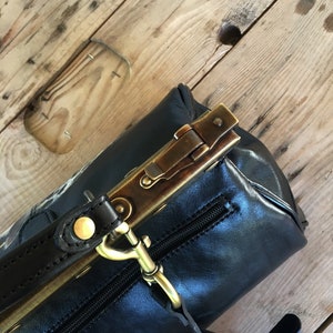 May include: A black leather handbag with a brass clasp and a brown leather strap. The bag has a zipper closure and a small pocket on the front.