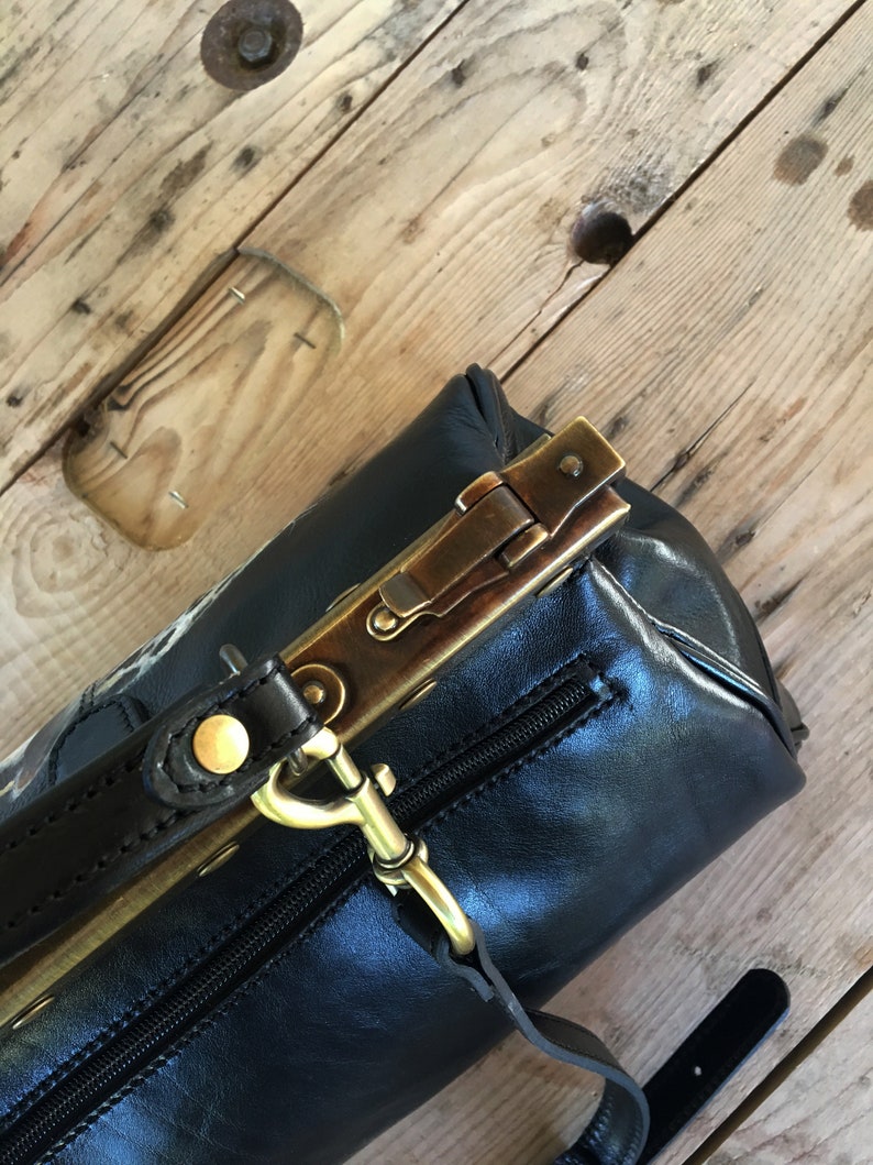 May include: A black leather handbag with a brass clasp and a brown leather strap. The bag has a zipper closure and a small pocket on the front.