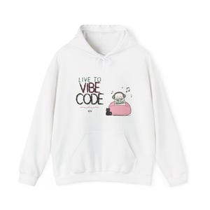 Op de afbeelding: Een witte hoodie met een grafische print met de tekst "LIVE TO VIBE CODE" boven een kleine illustratie van een personage met een koptelefoon op een roze zitzak met een zwarte kat en een code-symbool eronder.