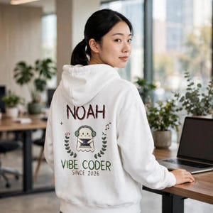 Könnte beinhalten: Ein weißer Kapuzenpullover mit einem Aufdruck auf der Rückseite, der den Text NOAH, VIBE CODER und SINCE 2026 zeigt. Das Motiv zeigt ein Comic-Gespenst mit Kopfhörern, das einen Laptop hält, umgeben von kleinen Zweigen und Musiknoten.