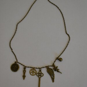 May include: A bronze necklace with multiple charms, including a key, a gear, a wing, a fairy, and a compass.