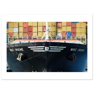 May include: The bow of the black container ship MSC IRENE features white lettering and a central logo with the letters msc. Stacks of yellow, red, and blue shipping containers are visible behind the ship's deck and white mast structure.