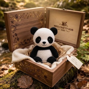 Könnte beinhalten: Ein gehäkeltes Panda-Spielzeug aus schwarzem und weißem Garn sitzt in einer offenen Holzschatulle. Der Deckel ist mit goldenen Symbolen graviert und innen steht der Text MISS CRAFTY HUB. Ein Anhänger trägt die Aufschrift TO A SPECIAL CRAFTER.