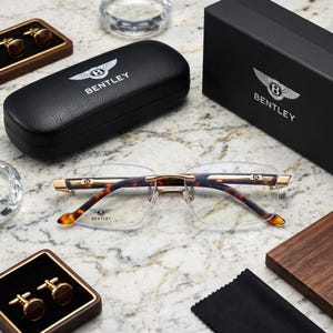 Può includere: Occhiali senza montatura con aste in metallo dorato e terminali con motivo tartarugato marrone. Le lenti presentano il logo e la scritta Bentley. Sono inclusi una custodia rigida nera con texture in pelle e una scatola nera con il logo.